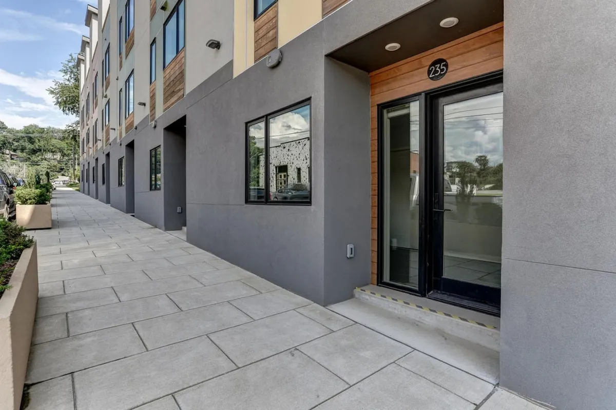 An exterior shot focusing on the entrance door, windows, and adjacent sidewalk, suggesting a modern, welcoming first impression upon arrival.