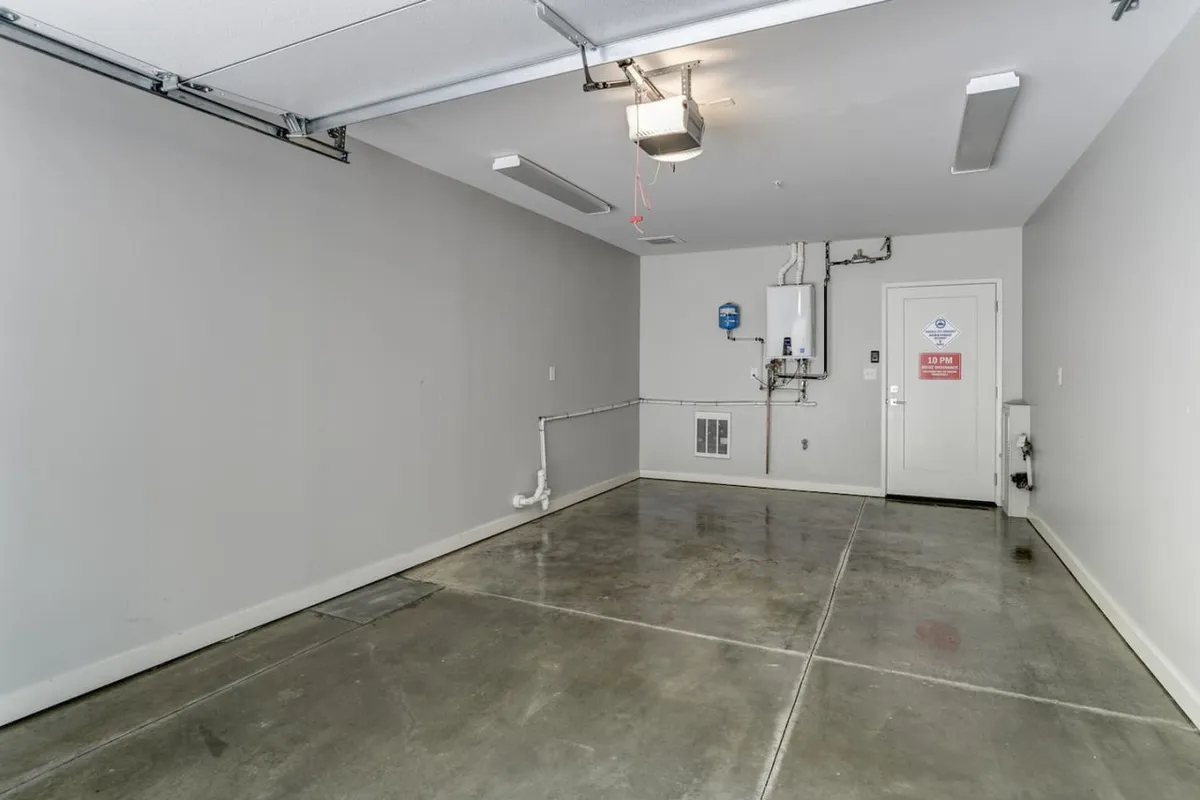 This image shows a private garage interior, featuring a garage door opener, a water heater, and an entry door. The space is neat and practical, clearly intended for secure vehicle parking and additional storage or workshop uses.