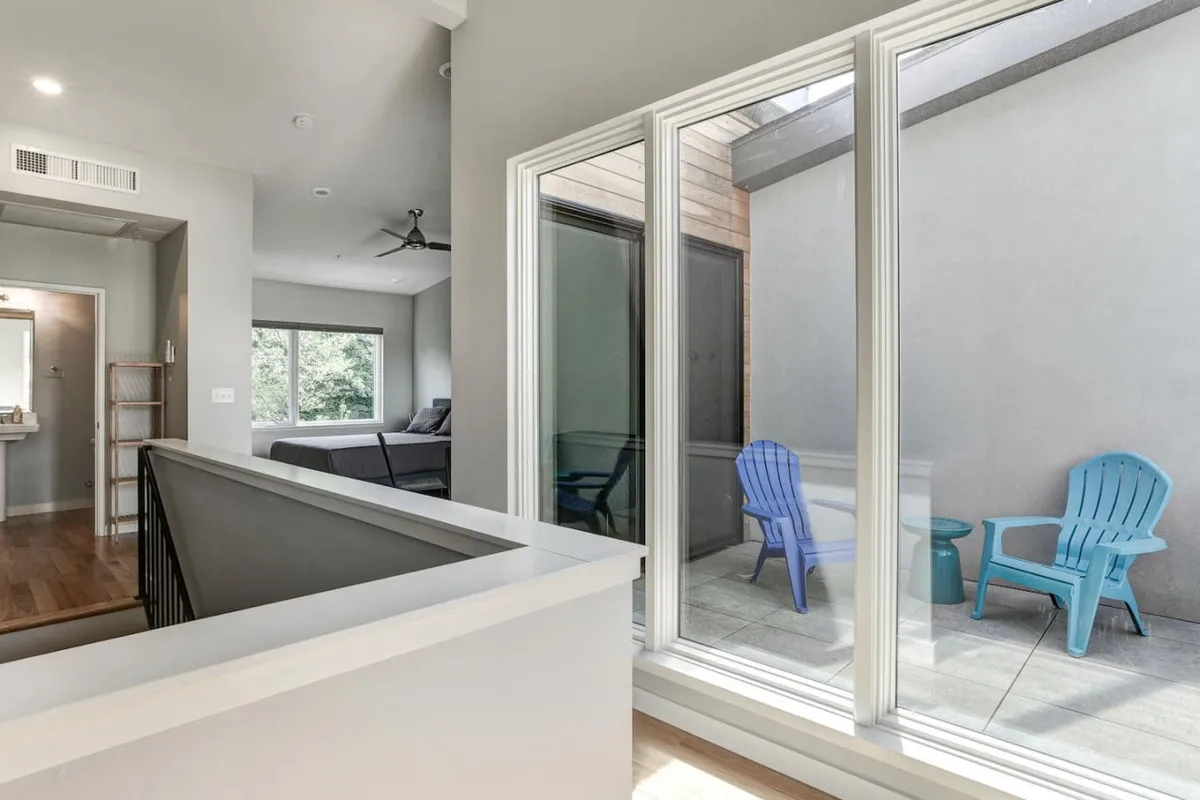 An open and airy interior space with large glass windows and blue chairs, creating a seamless connection between indoors and outdoors. The expansive windows offer a glimpse of views beyond, suggesting the mountain and city skyline vistas described in the section. The mood is calm and inviting, perfect for relaxing or socializing.