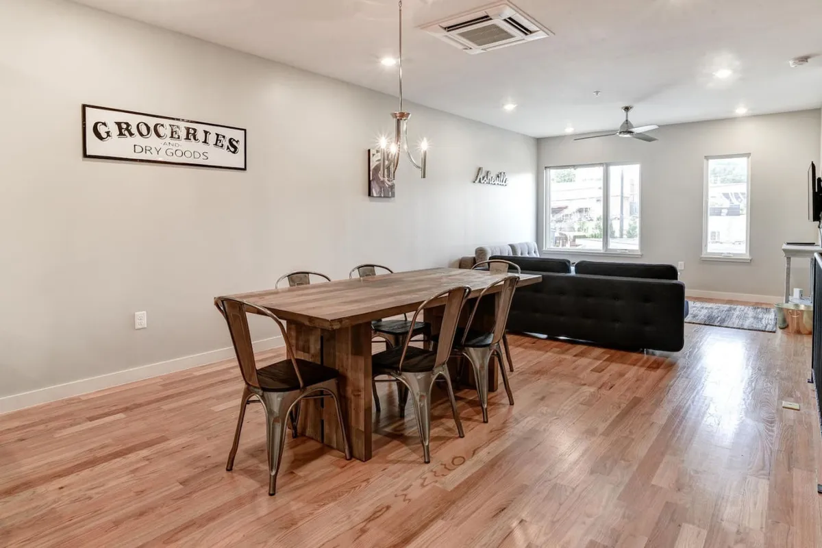 A wide-angle view of an open-concept living and dining area. The dining table is set for a meal, with a comfortable sofa nearby. Large windows flood the space with natural light, while tasteful light fixtures add warmth and ambiance.