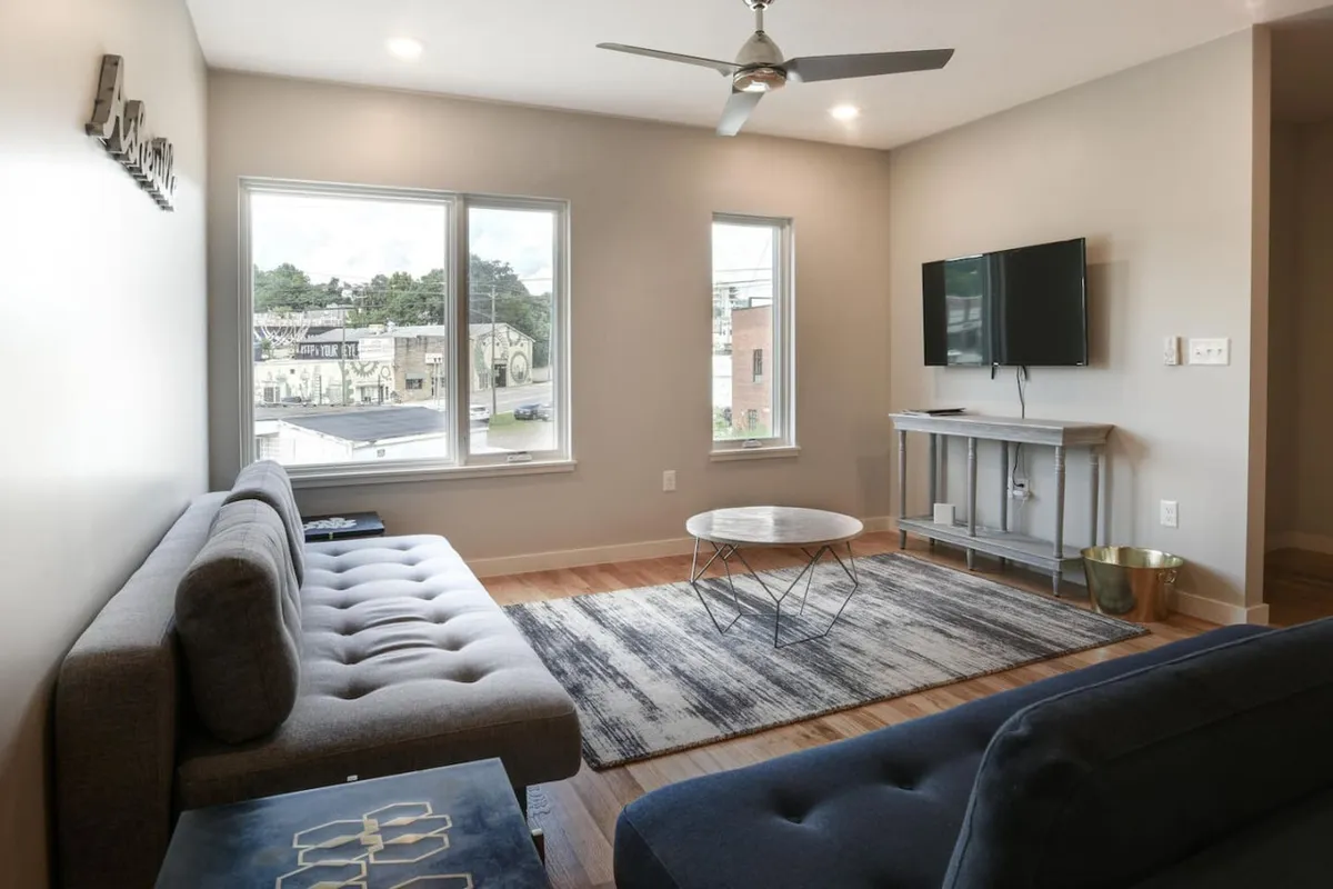The image showcases a contemporary living space with a comfortable sofa, a coffee table for games or snacks, a TV, and large windows that bring in natural light. The arrangement creates a cozy atmosphere for relaxing with loved ones after exploring the city.