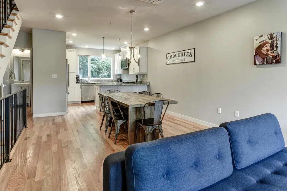 An open-concept space that seamlessly connects a spacious dining table, a plush sofa, and a modern kitchen area with a visible staircase. The setup is ideal for group meals, game nights, and casual gatherings, underscoring the home's flexibility for social occasions.