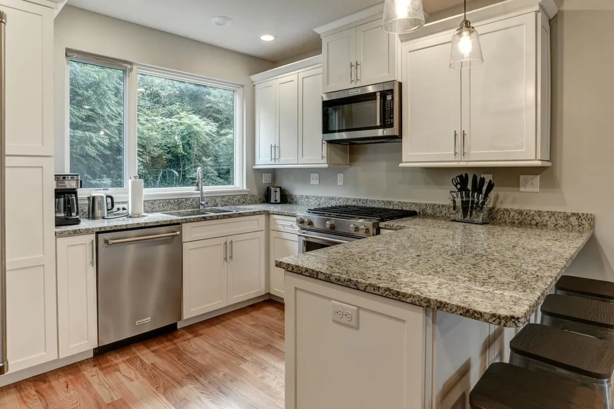 A modern kitchen with large windows, ample natural light, sleek appliances, and an open layout ideal for gatherings, with visible pathways for easy movement.