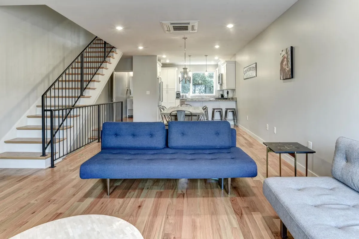 This image shows a welcoming open-plan living area featuring a blue sofa, a stylish staircase, and a kitchen island. The scene is set for socializing, relaxing, and enjoying meals together, offering a glimpse of the spacious, modern environment guests encounter upon arrival.